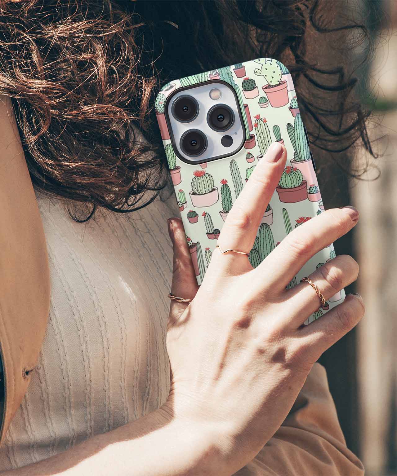 IPhone with pastel green case featuring various cartoon cacti in pots. - Cazify Canada