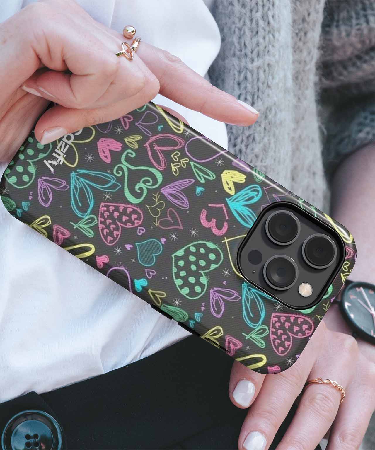 Black phone case with colorful doodle hearts design on an iPhone with triple camera lenses. - Cazify Canada