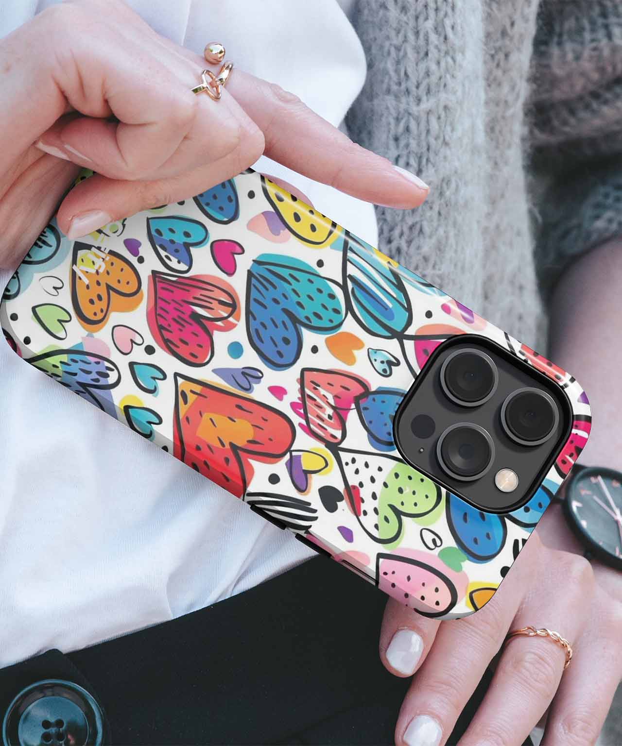 Colorful heart-patterned phone case with black-bordered camera cutout on iPhone held in hand. - Cazify Canada