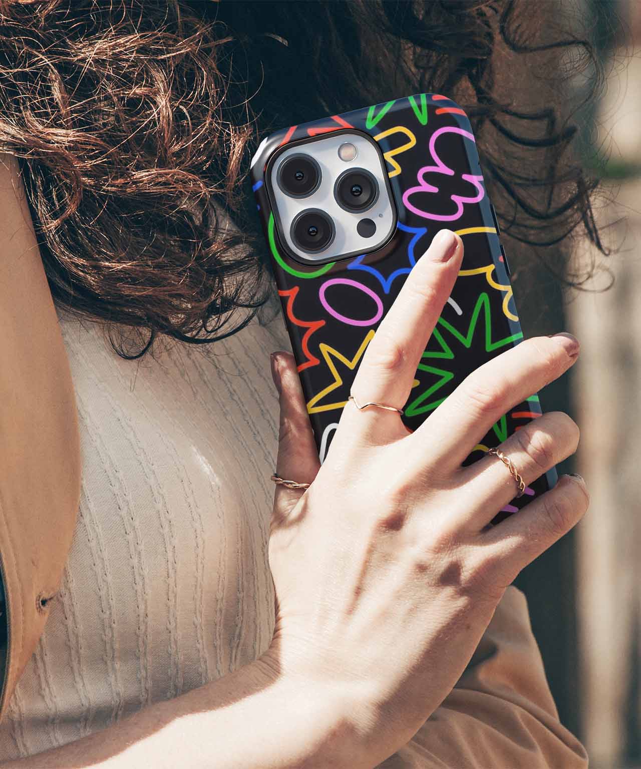 Black iPhone case with colorful abstract squiggles held by a woman with curly hair and light sweater. - Cazify Canada