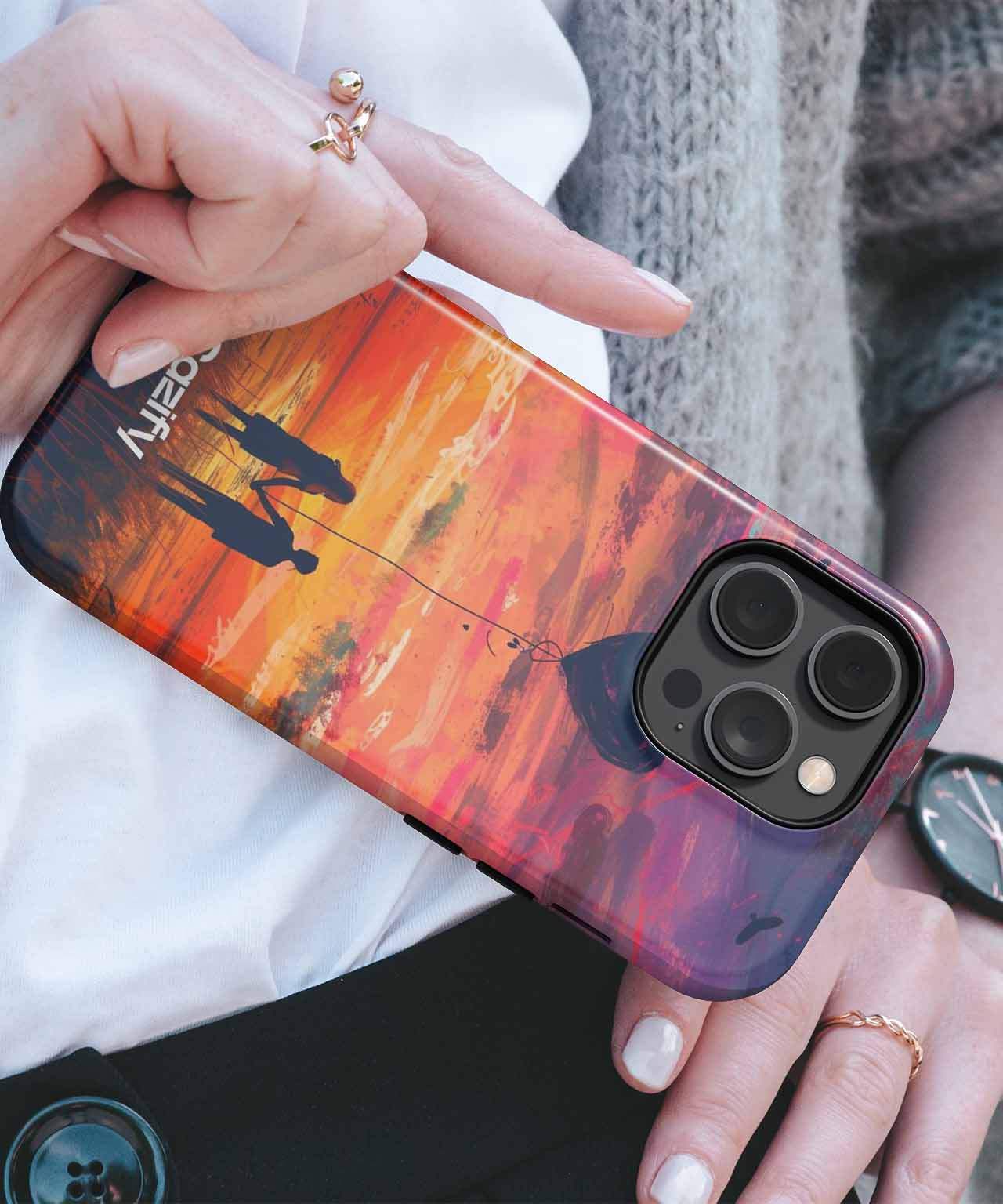 IPhone with sunset-themed case featuring silhouetted couple and vibrant orange and purple sky. - Cazify Canada