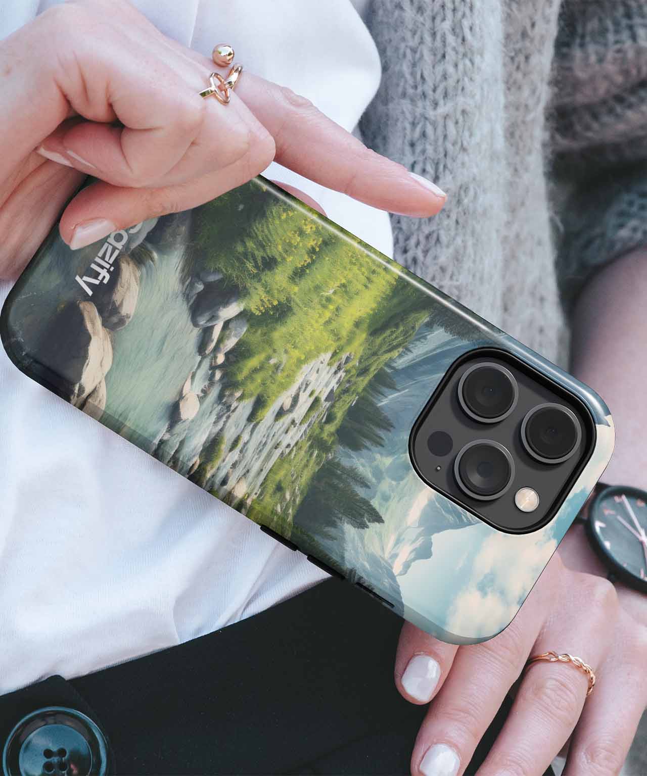 Cazify Canada - Hand holding iPhone with green forest landscape case and triple camera lenses.