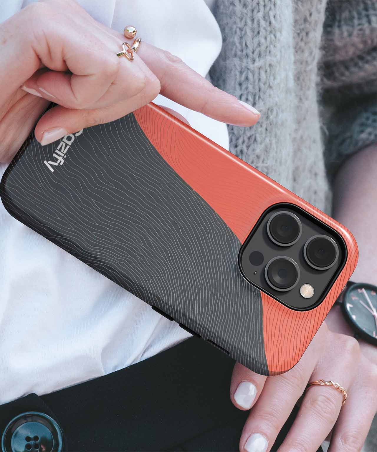 Black and orange textured phone case with raised camera protection on an iPhone held by a hand with rings. - Cazify Canada