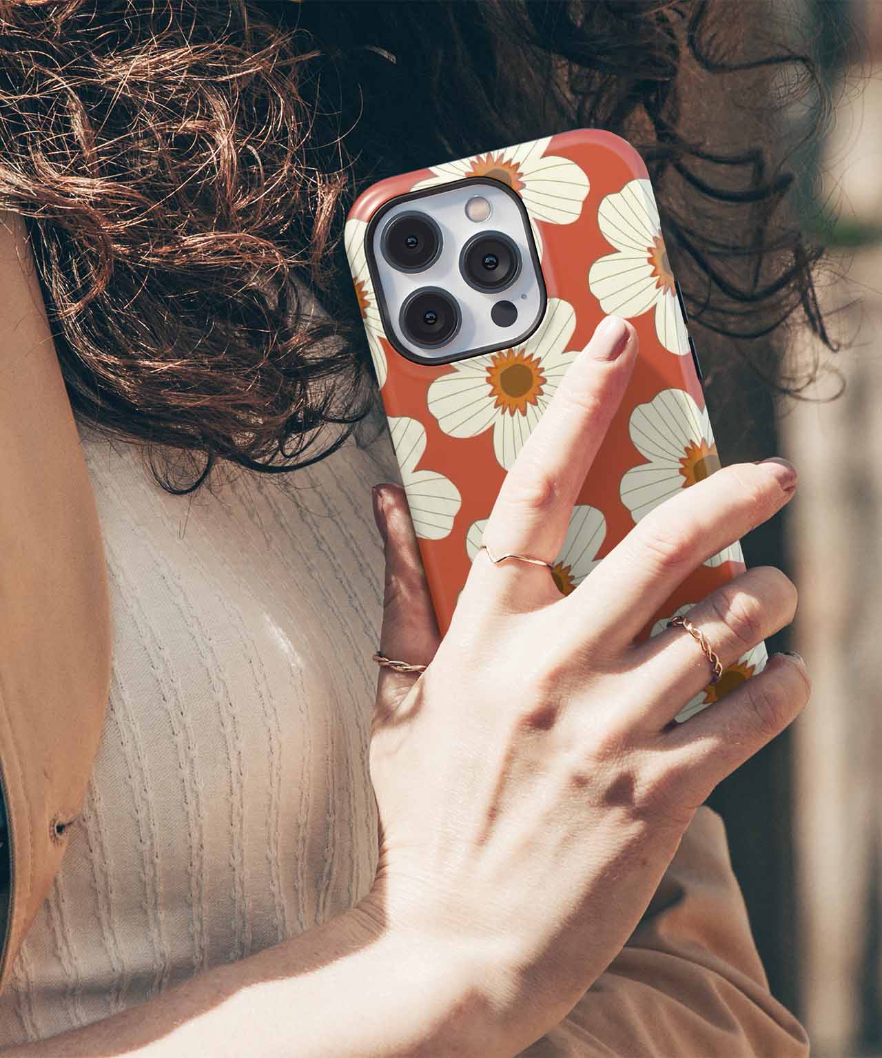 Cazify Canada | Art-Inspired iPhone Cases, Uniquely You! - Terracotta iPhone case with white floral pattern held by a hand with gold rings. - Charming Floral Fiesta on Terracotta iPhone case