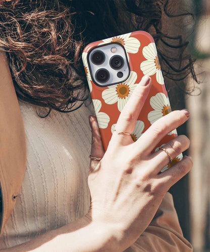 Cazify Canada | Art-Inspired iPhone Cases, Uniquely You! - Terracotta iPhone case with white floral pattern held by a hand with gold rings. - Charming Floral Fiesta on Terracotta iPhone case
