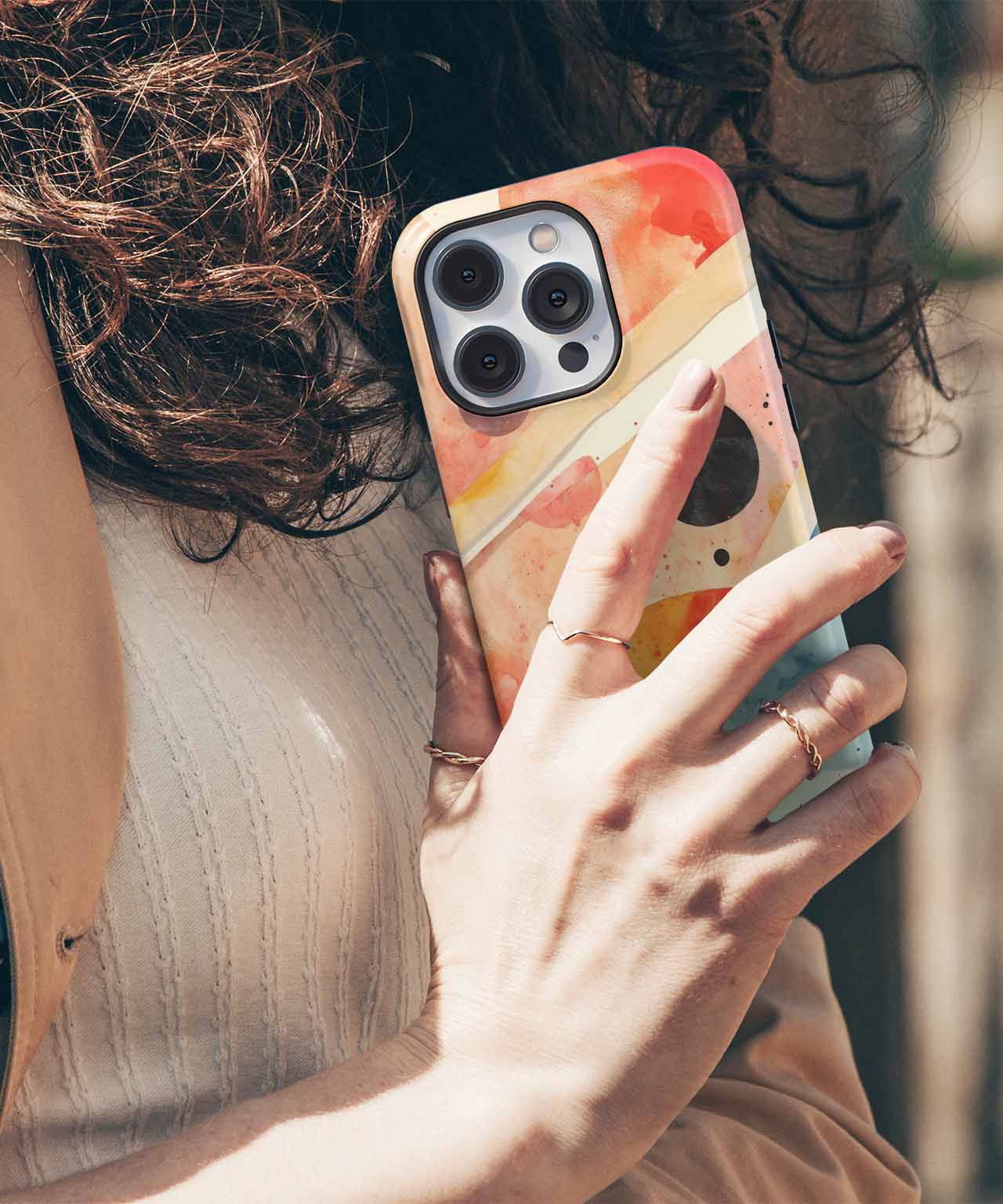 Hand holding iPhone with orange and cream abstract patterned case and visible triple camera lenses. - Cazify Canada
