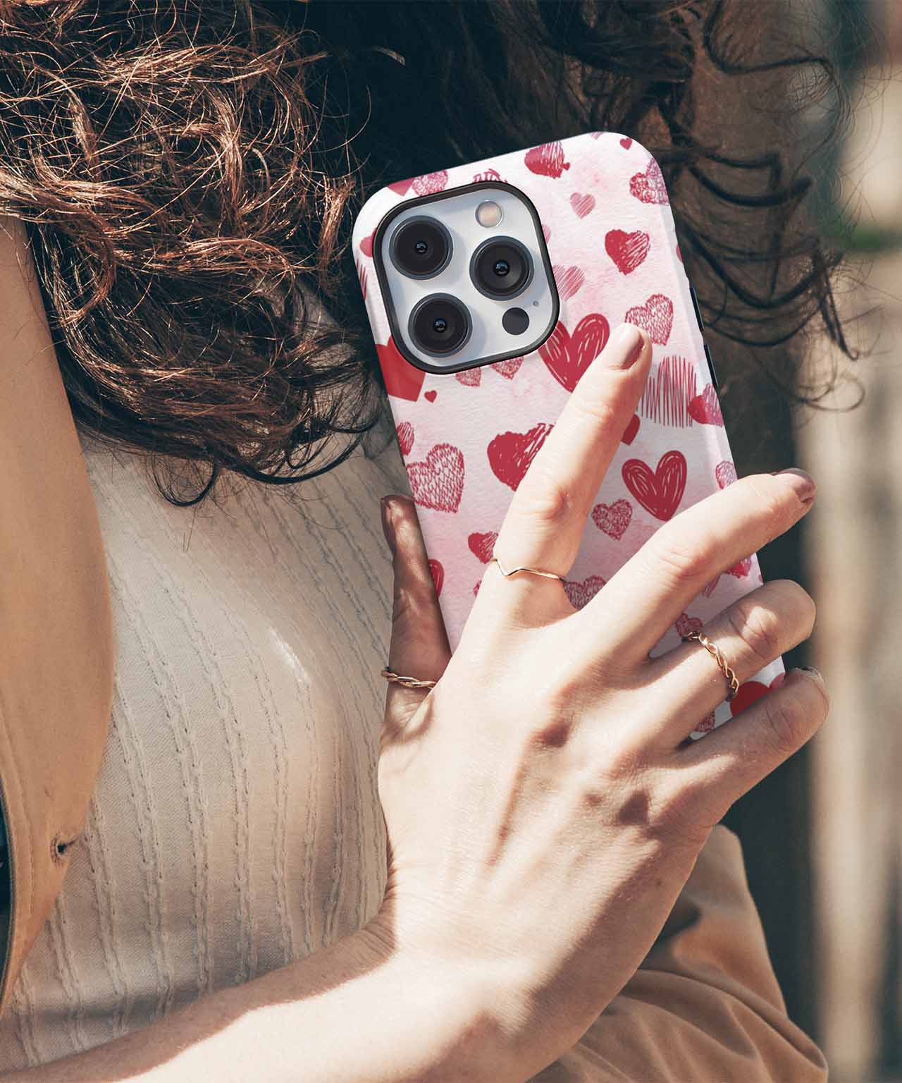 Phone case with pink hearts pattern on a silver iPhone with triple camera and white nail polish hand. - Cazify Canada