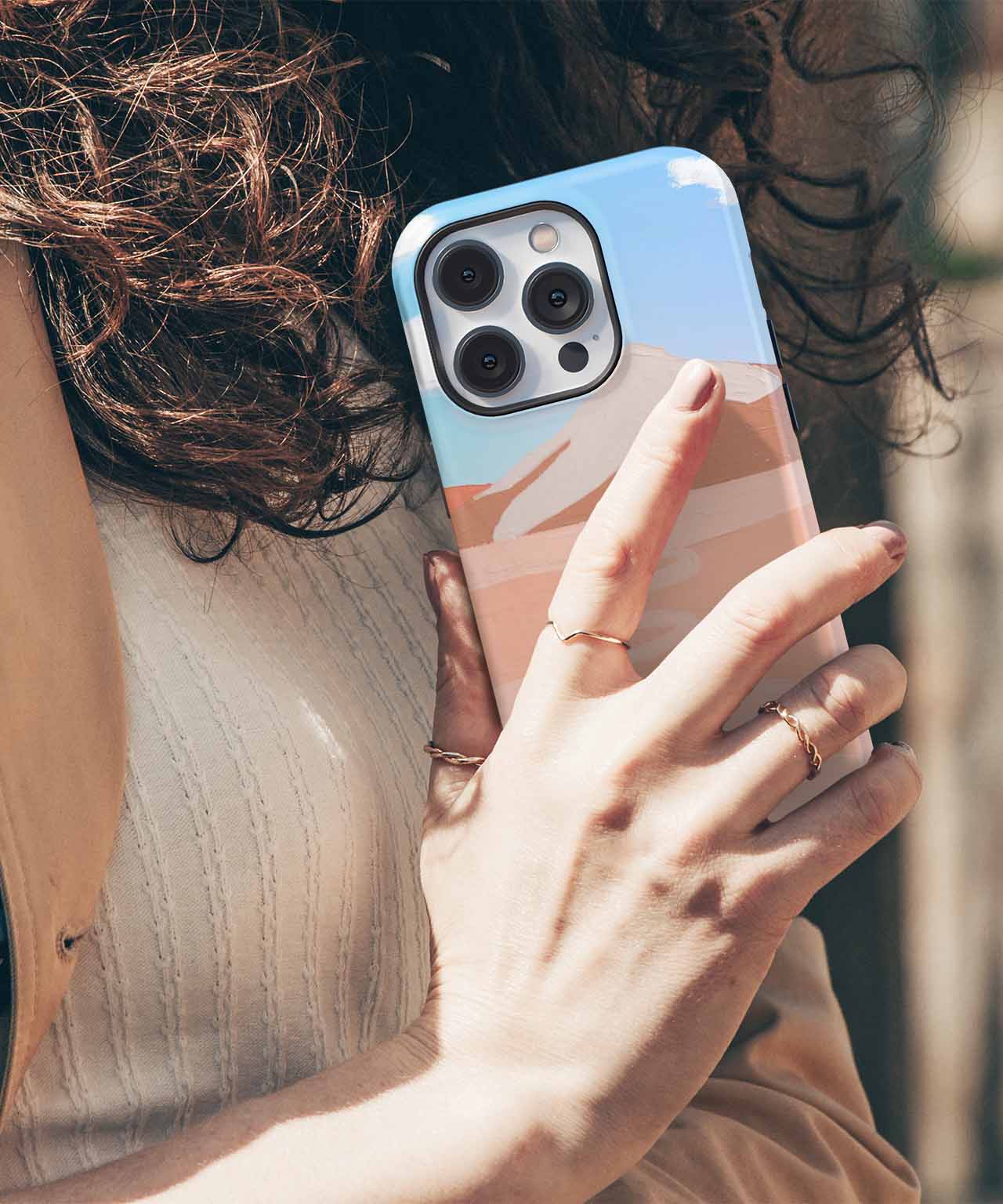 Cazify Canada - Hand holding iPhone with a pastel blue and beige abstract wave pattern case, triple camera lenses visible.